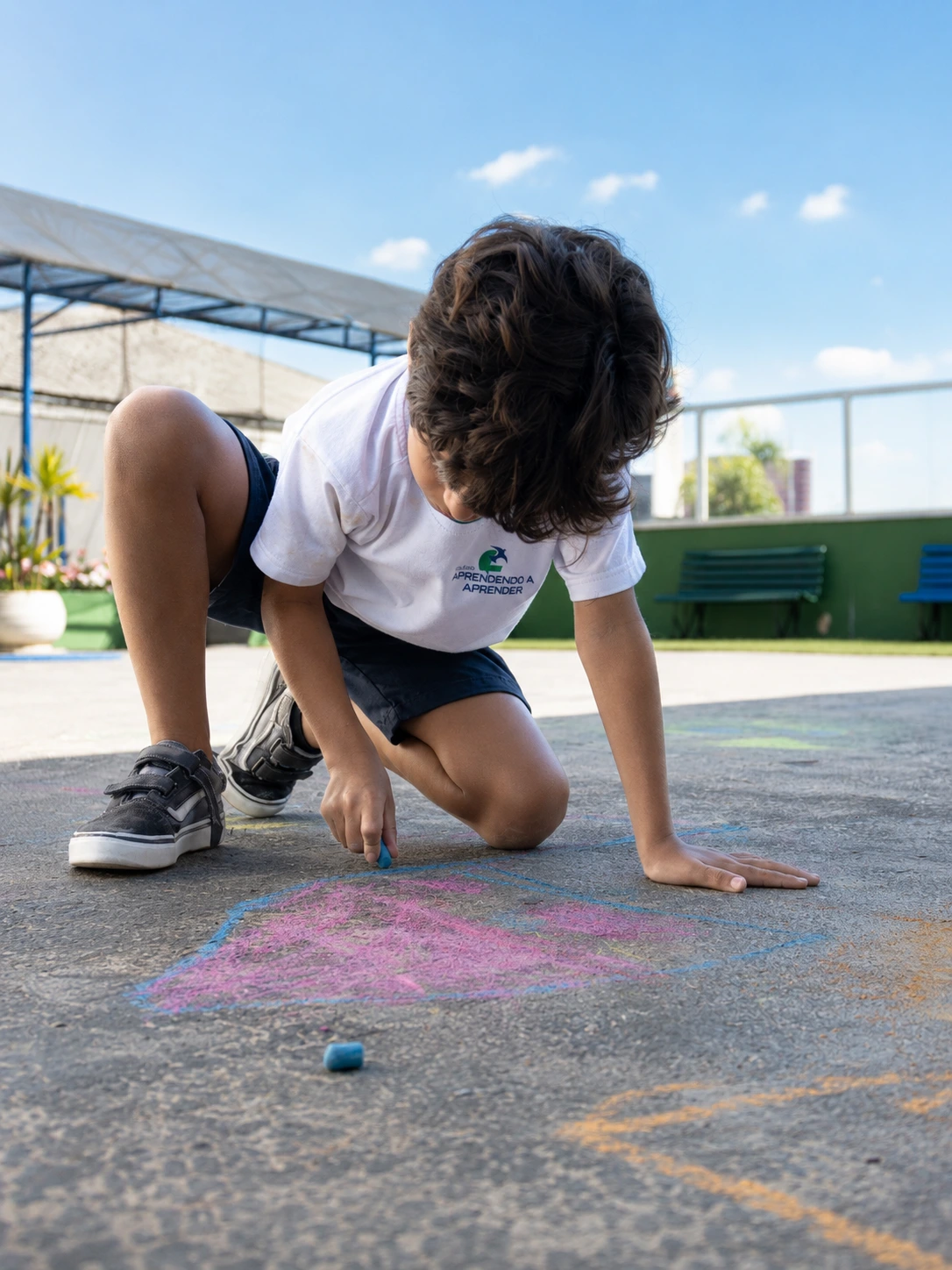 Criança desenhando com giz colorido no pátio da escola.