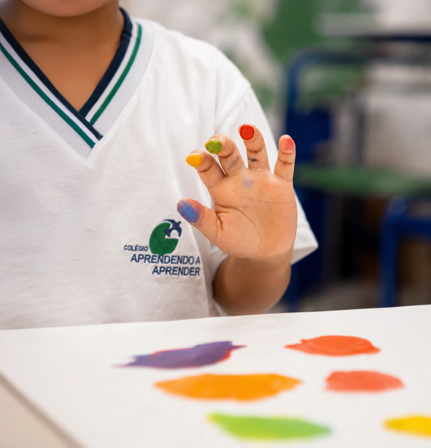Criança do Colégio Aprendendo a Aprender mostra os dedos pintados de várias cores.