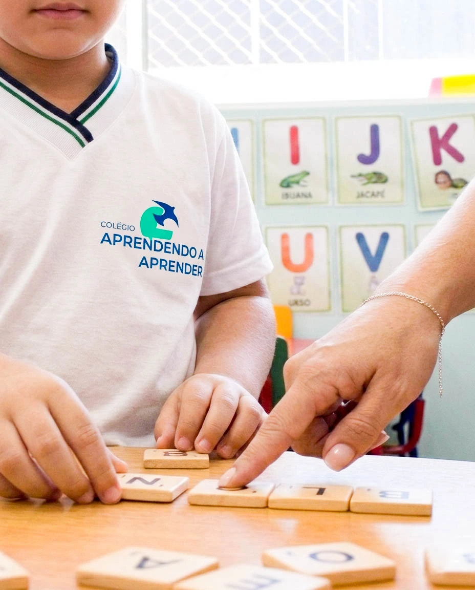 Criança com uniforme da escola participa de uma atividade com materiais de madeira.